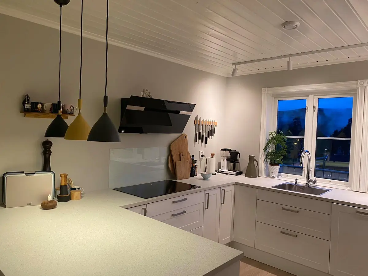 Hvitt kjøkken med lys benkeplate og pendellamper i gult og sort